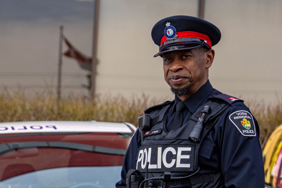 Police officer standing in front of a window with the reflection of a Canadian flag.
