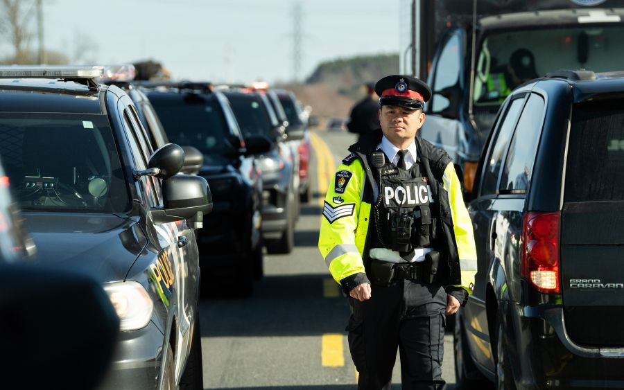 Police officer in reflective jacket walks between rows of cars.
