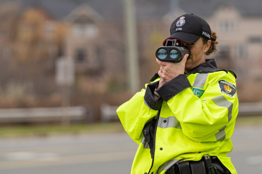 Police officer looks into a traffic radar along a road.