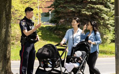 A man in a police uniform speaks to two people pushing strollers