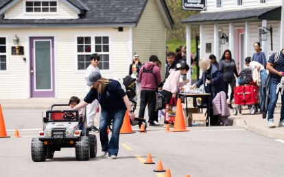 A man pushes a miniature car with a kid inside