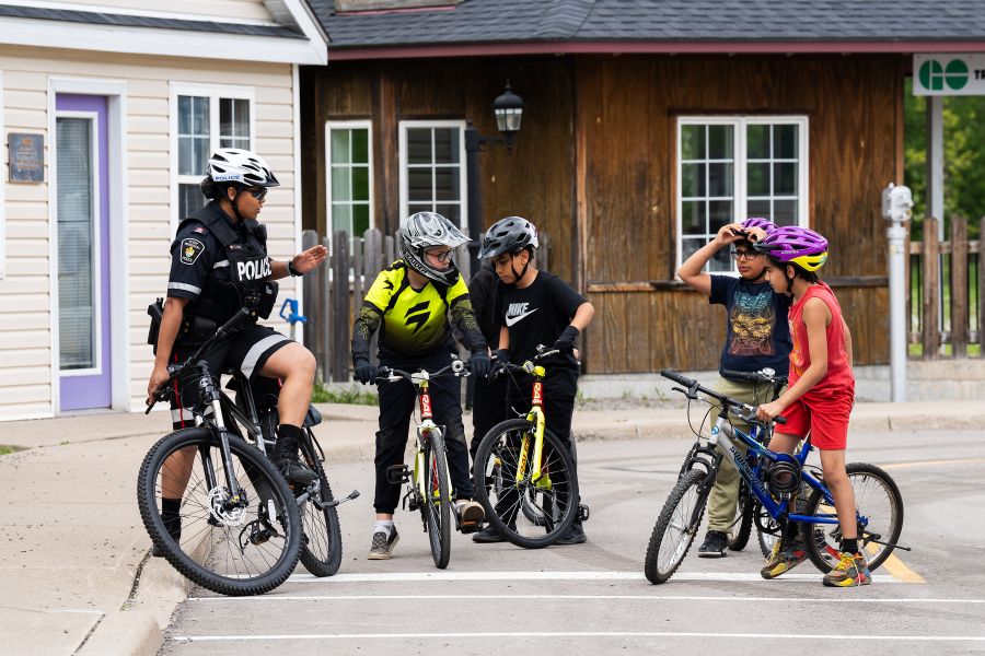 A woman in a police uniform on a bicycle talks to kids on bicycles