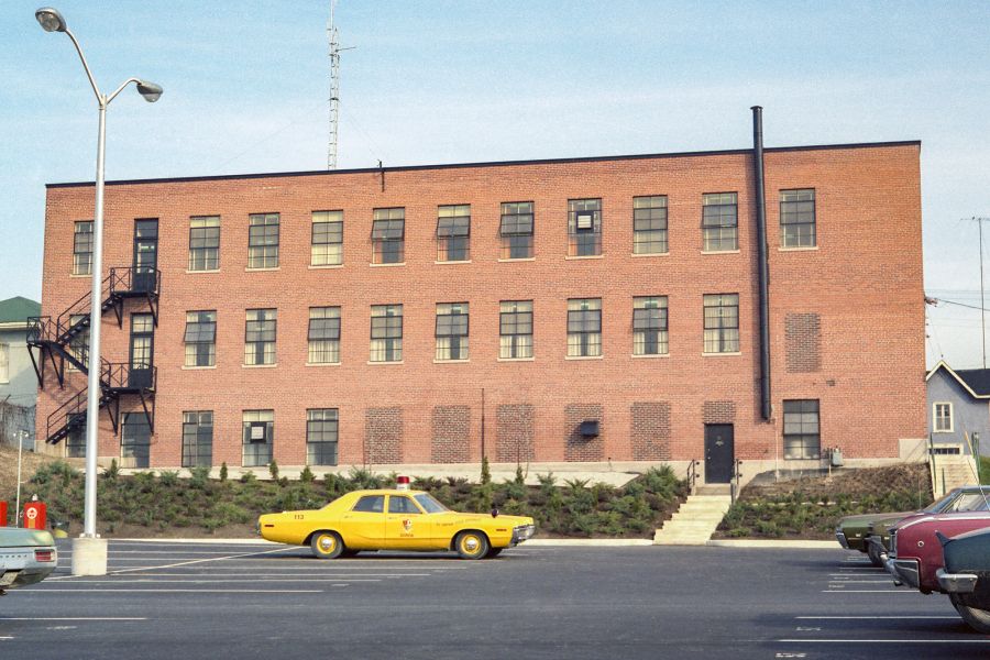 A yellow police cruiser sits in front of a red bricked building