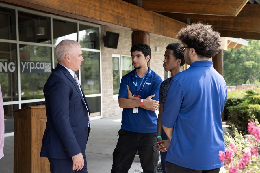 A group of teens in blue shirts speak to a man in a suit