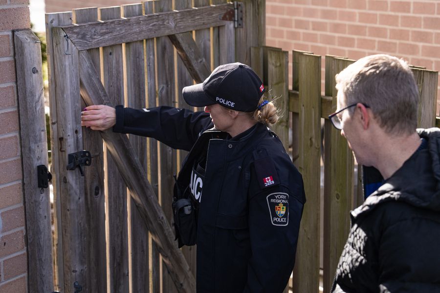 A police officer and a man look at a gate on the fence at a home