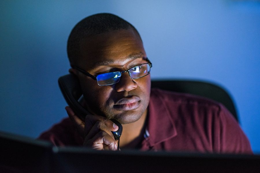 A man looks at a monitor while holding a phone to his ear