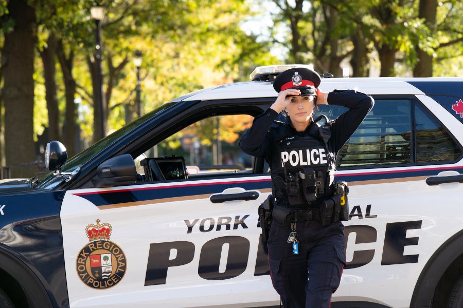 A woman in a police uniform walks in front of a police vehicle while adjusting her cap