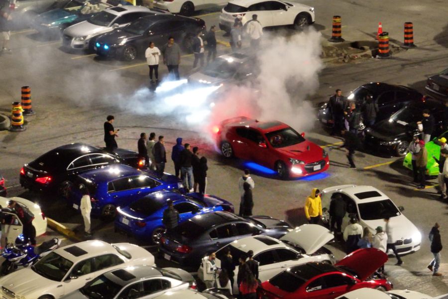 A car conducts a burnout in a plaza parking lot during a crowded car rally