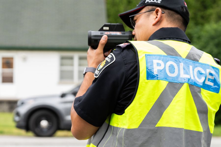A man in a vest that reads POLICE holds a radar device