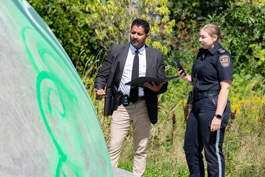 An officer in uniform and an investigator look at graffiti.
