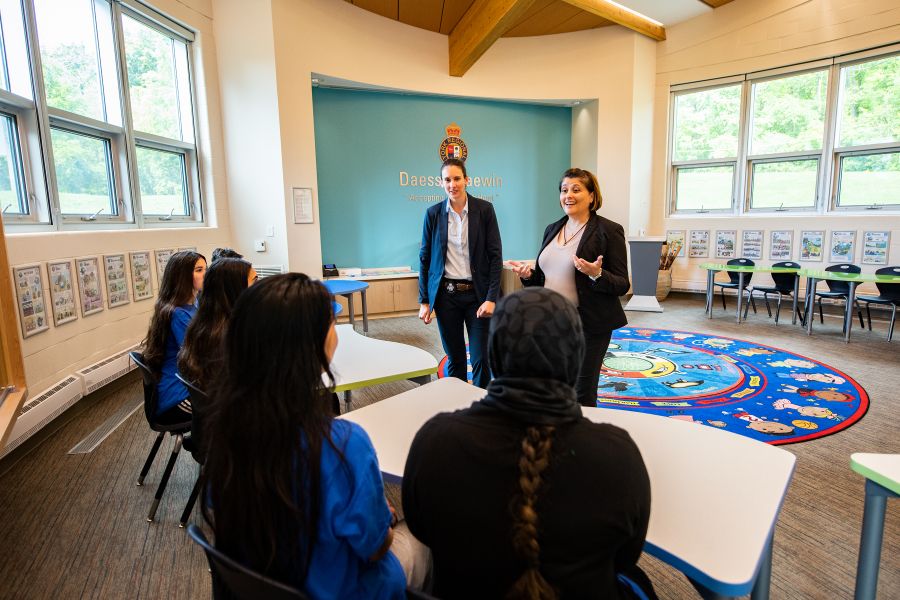 Two women in suits speak to a group at a table