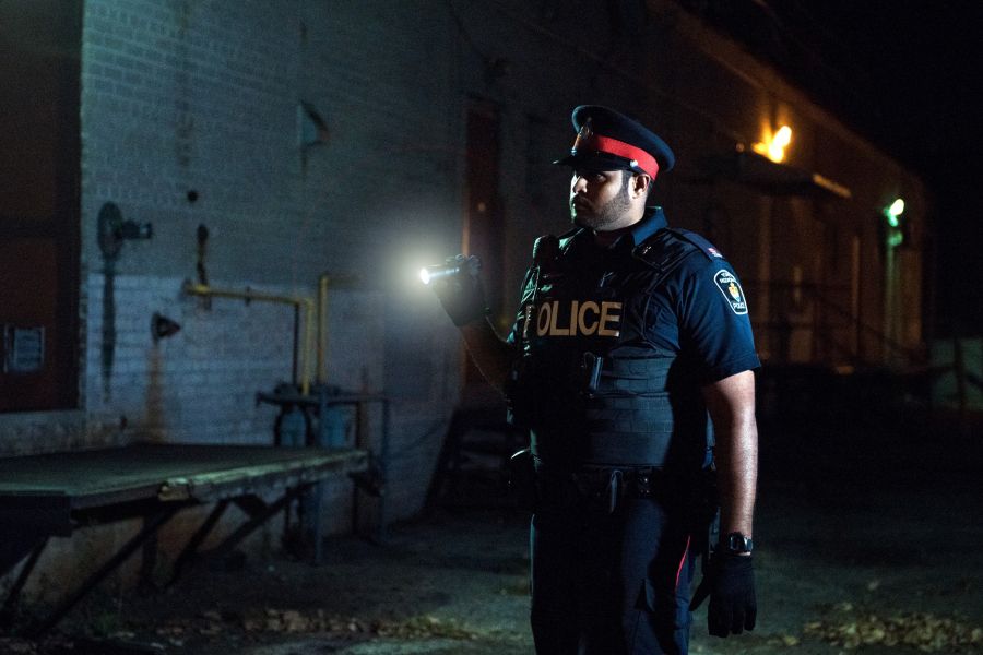 A police officer shines a flashlight in a dark alley