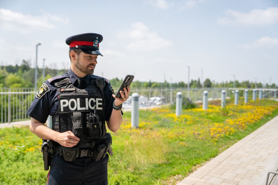 Police officer looking at phone outside on a sunny day.