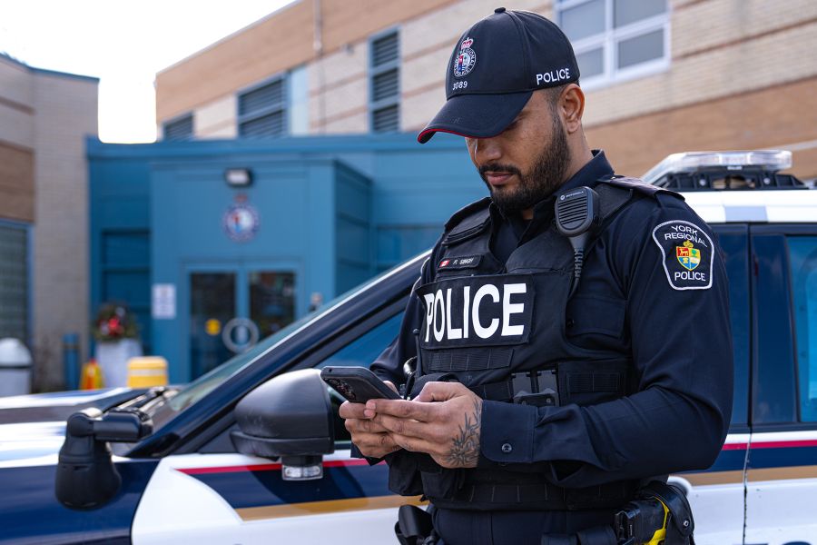 Police officer on phone in front of cruiser.