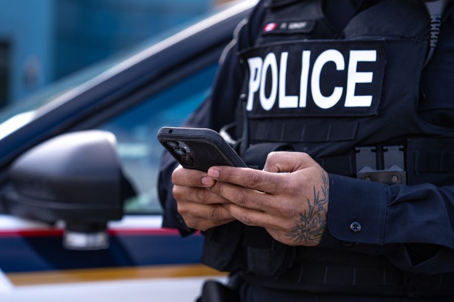 Close up of police officer typing on phone in front of cruiser.
