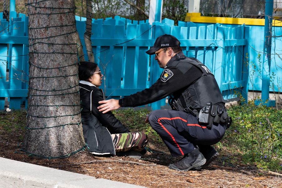 An officer speaks with a woman who is sitting under a tree