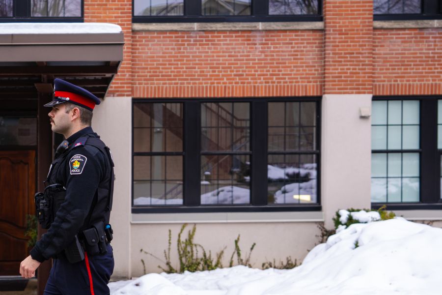 A police officer walking along the side of a building with windows.