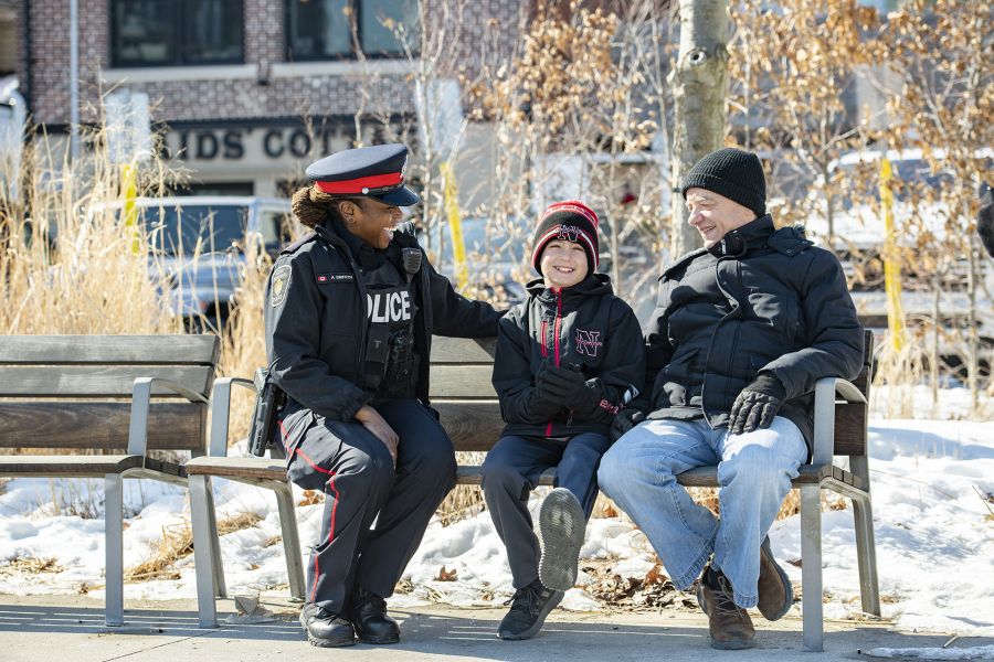 An officer sits on a bench with a man and a child