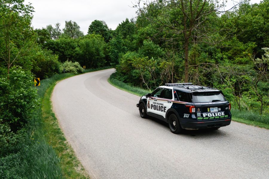 York Regional Police cruiser driving away on a path with a lot of green foliage.