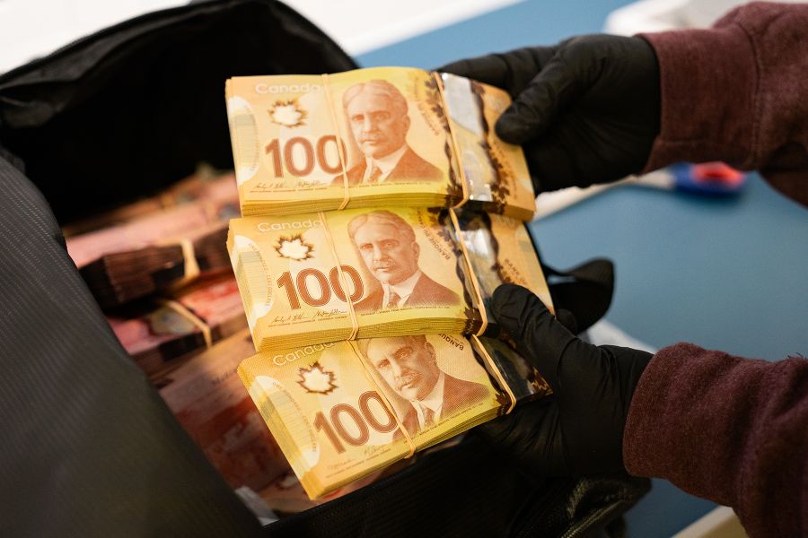 Someone wearing gloves holds stacks of hundred dollar bills.