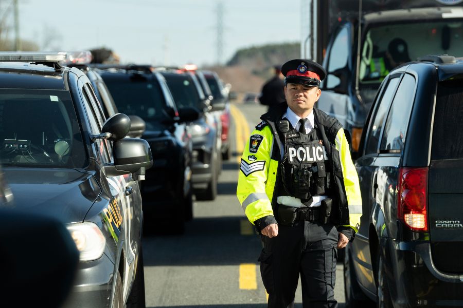 Police officer in reflective jacket walks between rows of cars.
