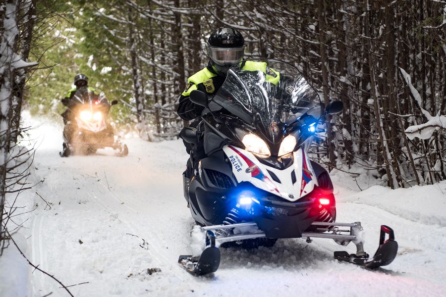 Officers drive snowmobiles down a snowy path