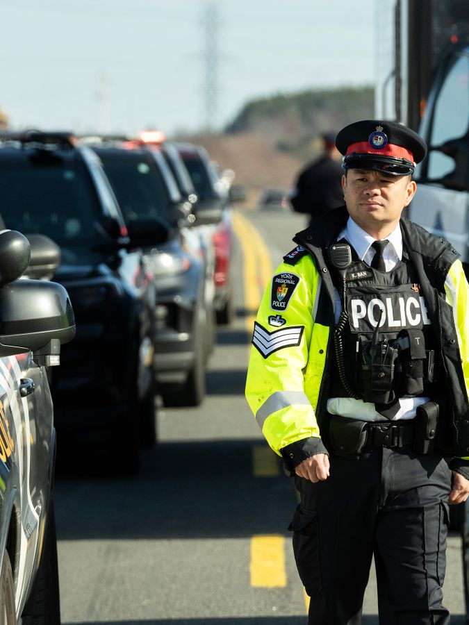 Police officer in reflective jacket walks between rows of cars.