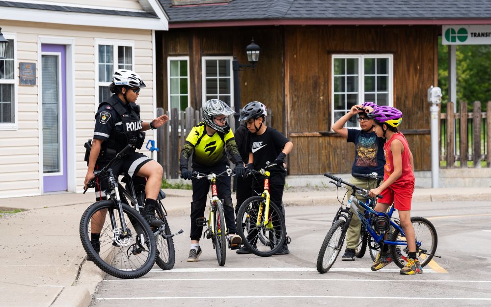 A woman in a police uniform on a bicycle talks to kids on bicycles