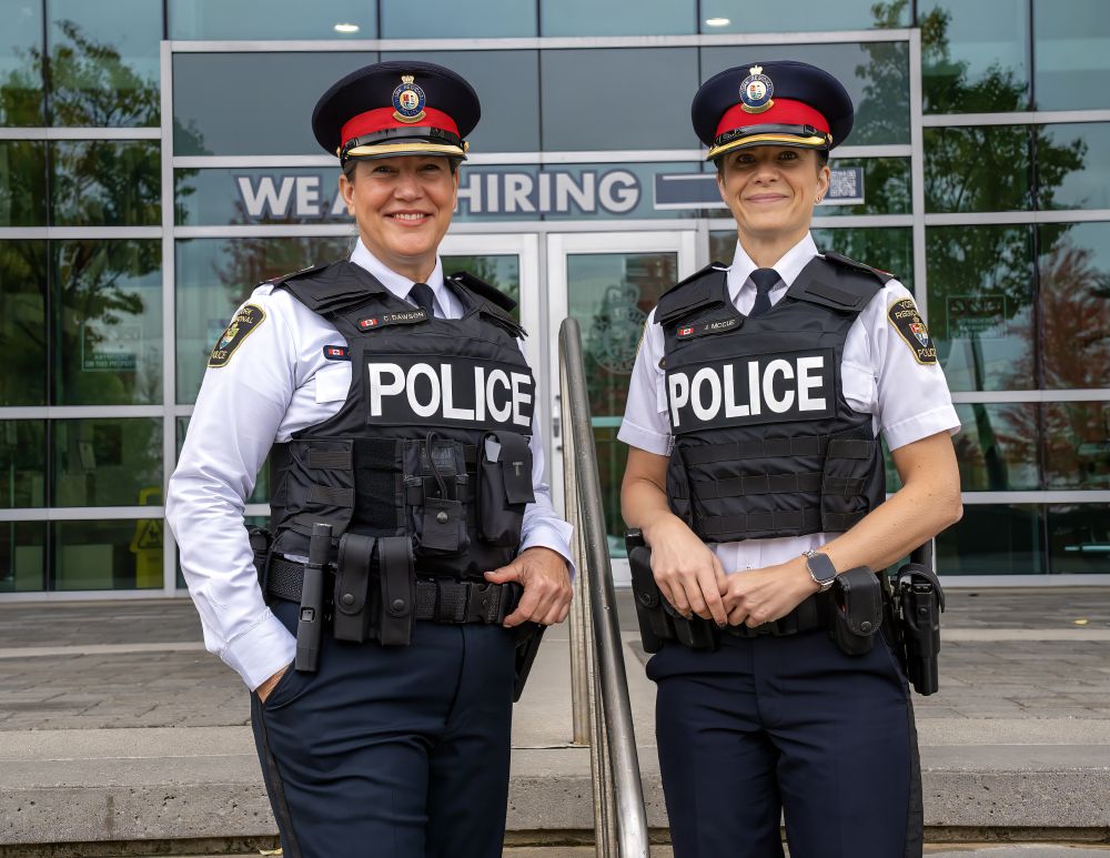 Two female police officers stand smiling in front of a building 