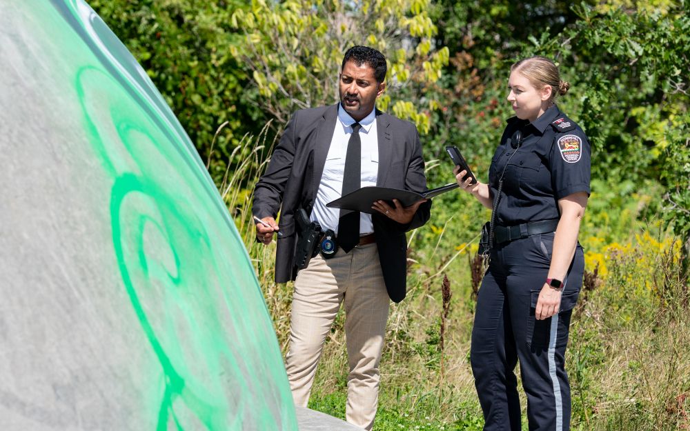 A man in a suit speaks to a woman in a uniform next to graffiti