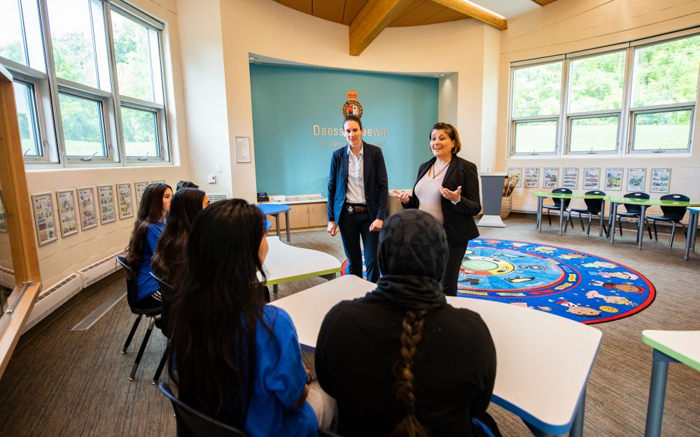 Two women in suits speak to a group at a table