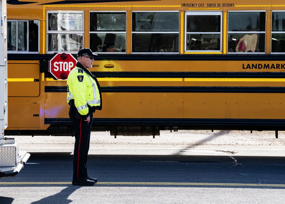 A man in a reflective jacket stands in front of a yellow school bus