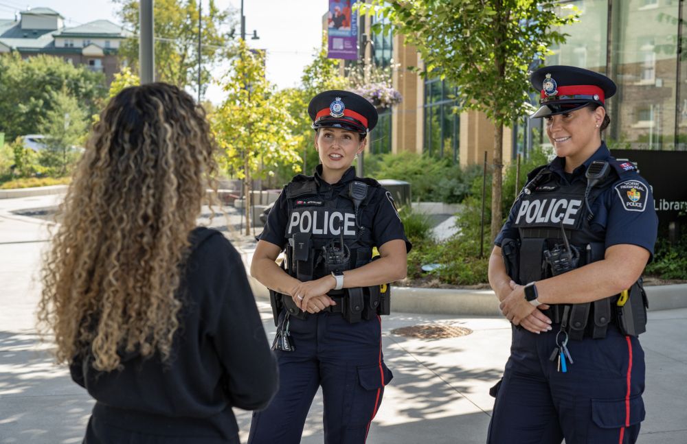 Two police officers speak with a civilian in an urban park.