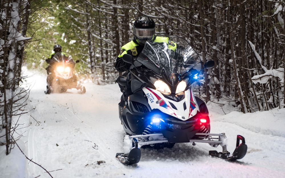 Officers drive snowmobiles down a snowy path