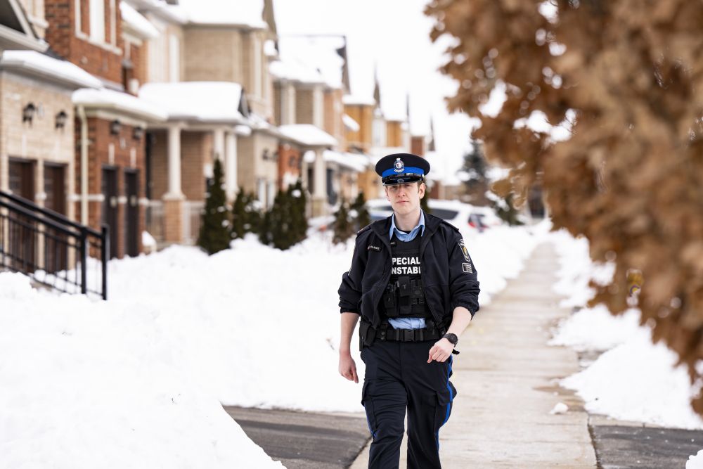 A man in a uniform walks on a snowy sidewalk