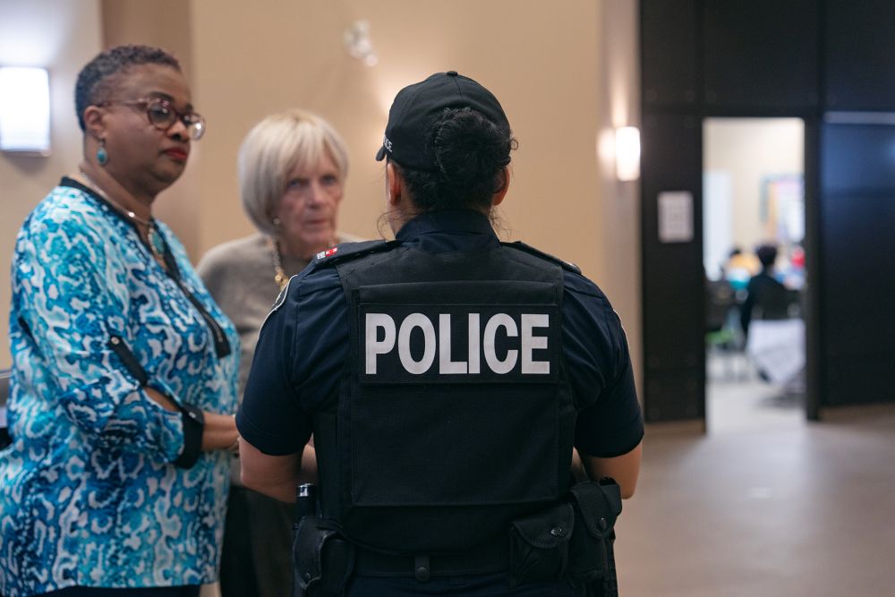 Police officer speaking to two women, classroom in distance.