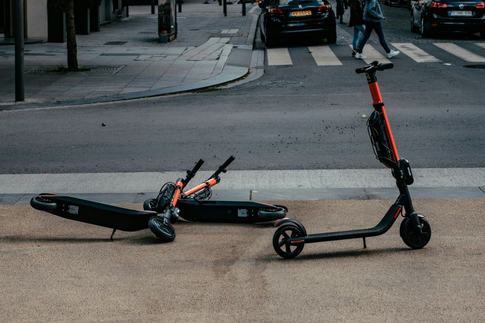 A photo shows three e-scooters on the side of a road.