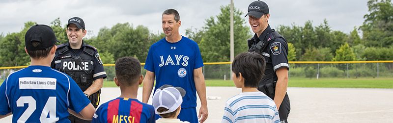Two officers in uniform with a group of kids and a coach of a baseball team